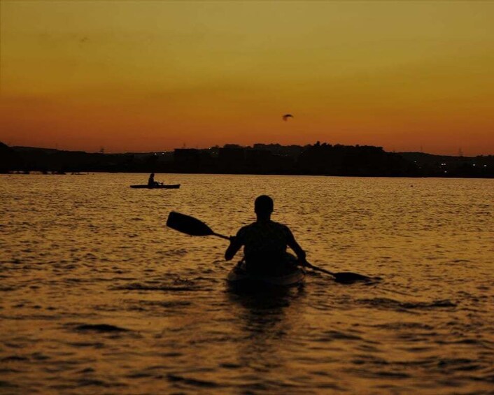 A silhouette of a person kayaking on a body of water during sunset. 1