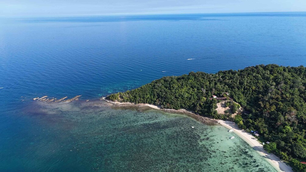 An aerial view of a coastal area with clear waters, a sandy beach, and a densely forested island. 1