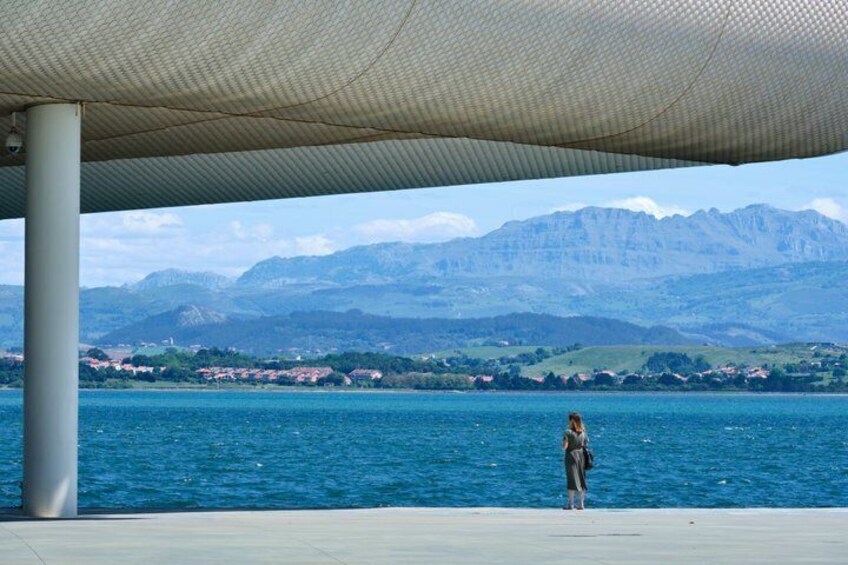 A person standing under a shelter by a lake with mountains in the background. 5