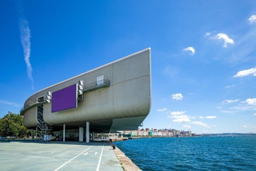 A futuristic building with a curved design, large windows, and a purple panel, situated by a waterfront with a clear sky. 4