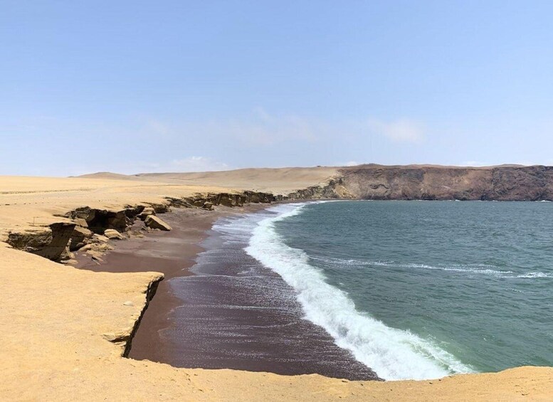 A coastal landscape with a sandy beach, rocky cliffs, and a clear blue sky. 1