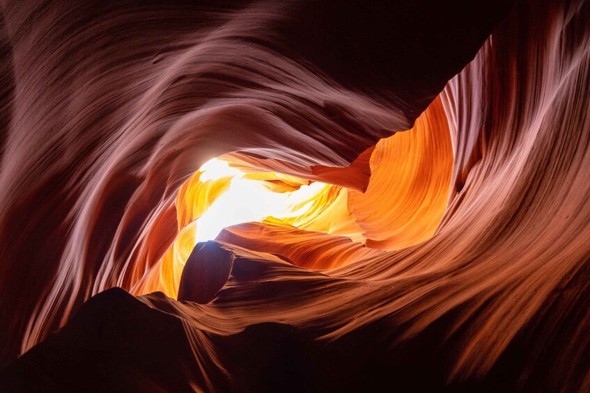 A canyon with smooth, flowing rock formations and a bright light source at the bottom. 5