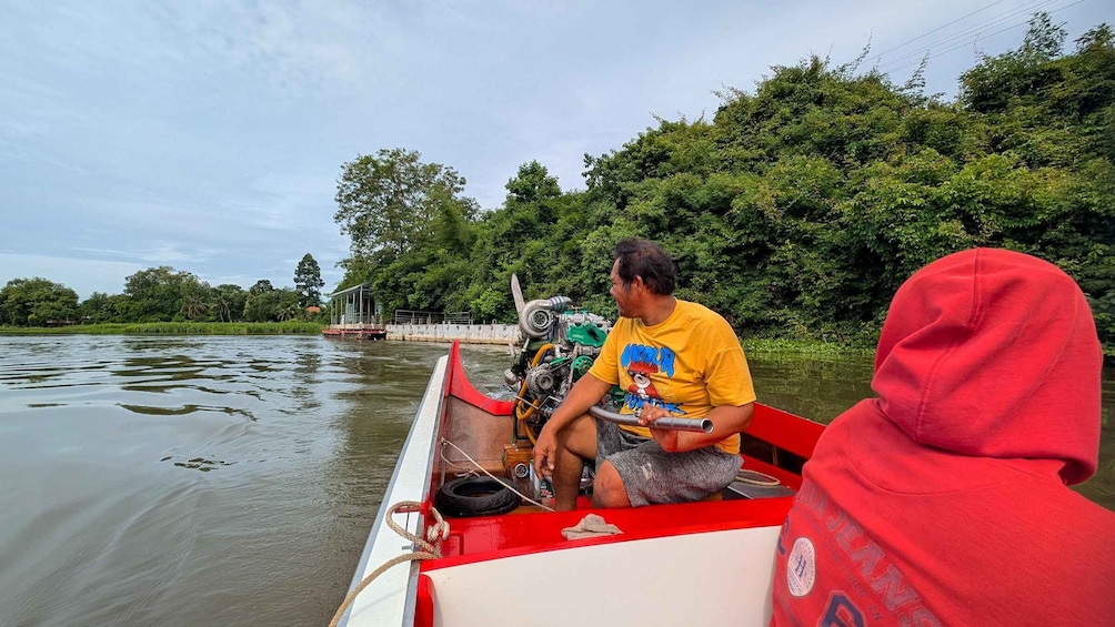 A man in a yellow t-shirt on a red boat with a motor, surrounded by calm water and greenery. 2