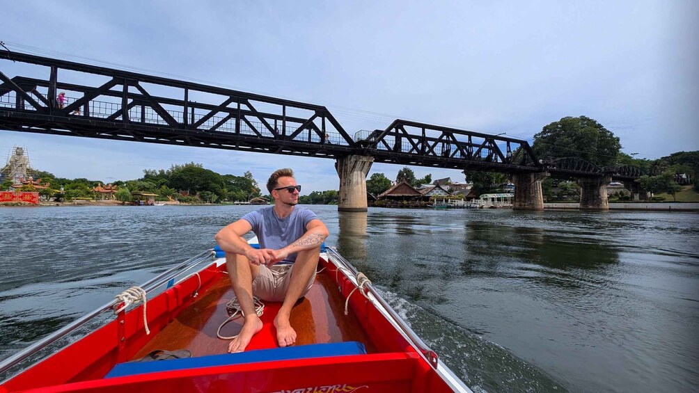 A man in a red boat on a river with a bridge in the background. 1