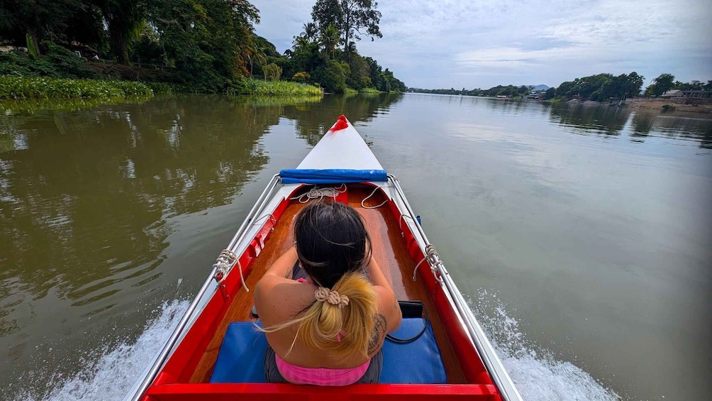 A person in a red and white boat on a calm river, surrounded by lush greenery and trees. 5