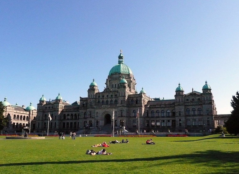 A large historic building with a prominent green dome and multiple smaller domes, surrounded by a well-maintained lawn with people relaxing. 2