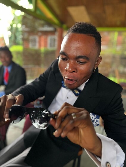A person in a black suit with a white shirt and blue bow tie, holding a smartphone. 5