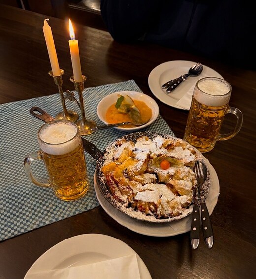 A meal with a fruit tart, beer mugs, a candle, and cutlery on a table. 3