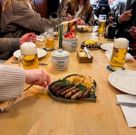 A group of people dining at a restaurant with a meal of sausages and sauerkraut, beer mugs, and a Deving cheese dish on the table. 2