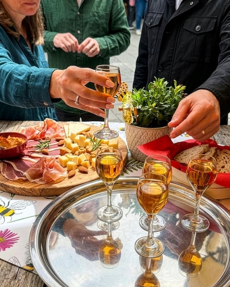 A group of people toasting with wine glasses at a table with cheese, bread, and a potted plant. 1