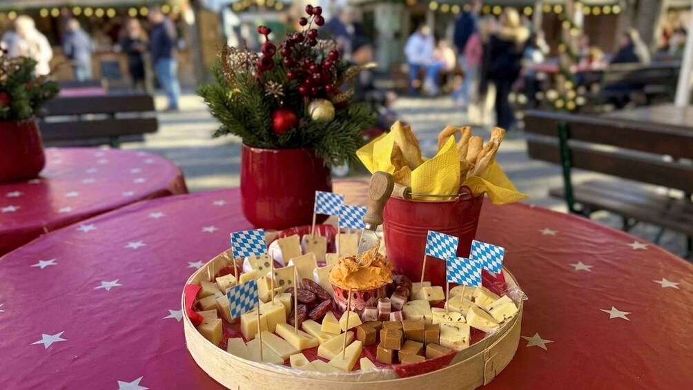 A wooden platter with various cheeses and crackers on a red tablecloth with star patterns. 5