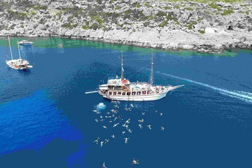 Un barco grande con varios pasajeros, fondeado en un mar azul cristalino con costas rocosas al fondo. 5