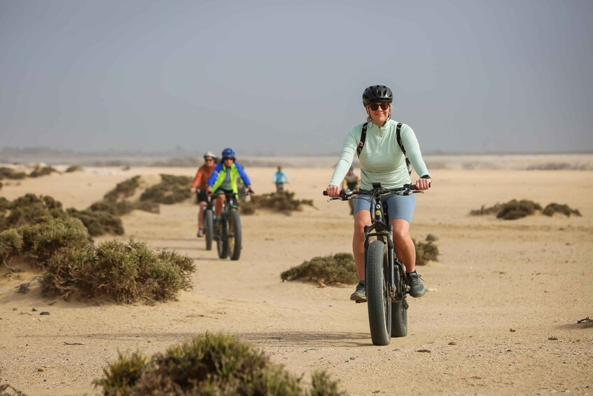 A person riding a bicycle on a sandy path with sparse vegetation. 3