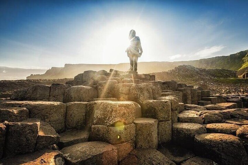 Una persona está de pie sobre bloques de piedra, con un paisaje iluminado por el sol al fondo. 5