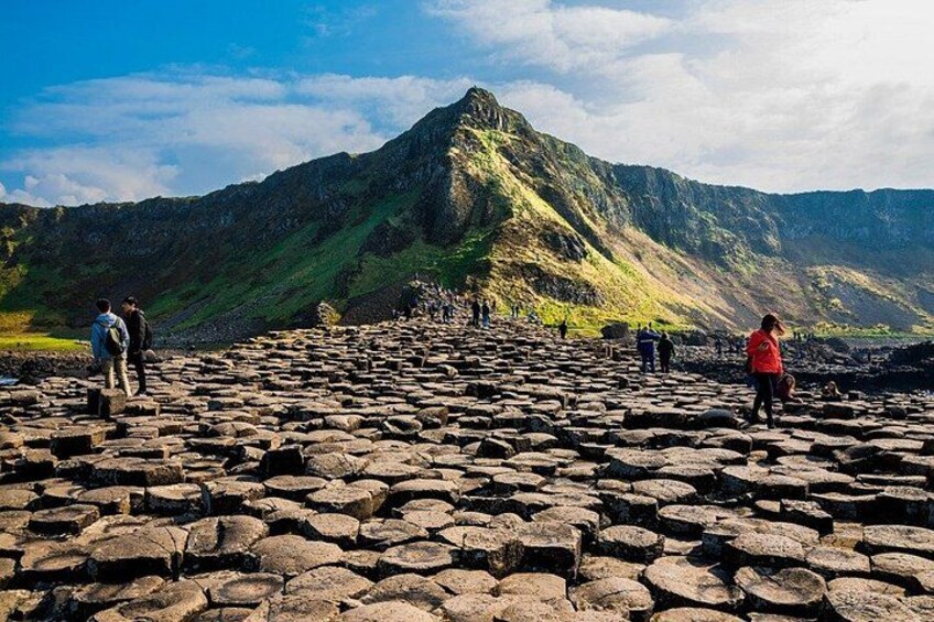 A rocky terrain with people walking, a mountain in the background, and a clear sky. 1