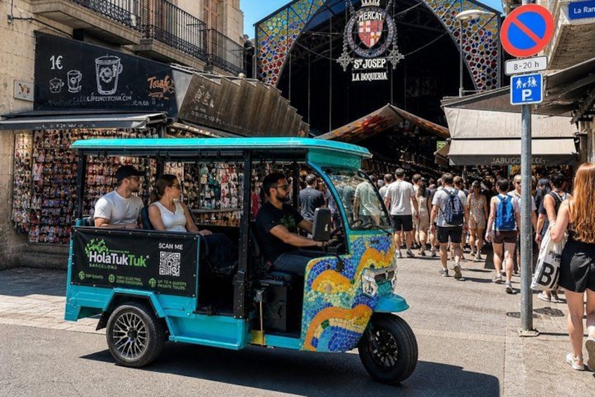 A colorful tuk-tuk with passengers, parked on a busy street with shops and a market in the background. 3