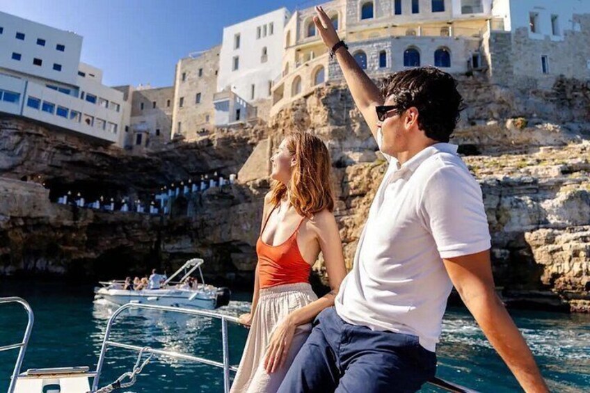 A couple on a boat with a rocky coastline and buildings in the background. 3