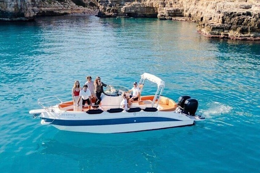 A boat with people on a clear blue sea, rocky cliffs in the background. 2