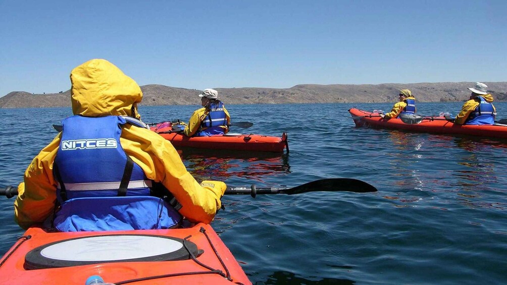 Three people kayaking on a calm body of water with a hilly landscape in the background. 3
