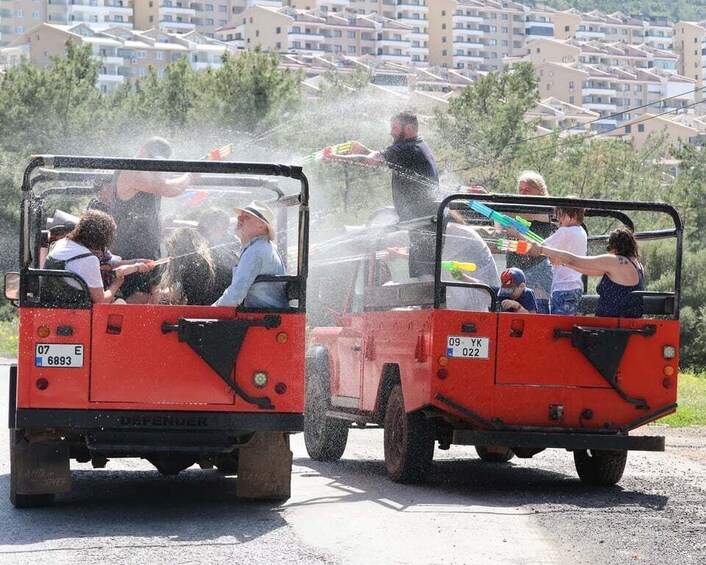 Two red jeeps with passengers spraying water from toy guns. 4