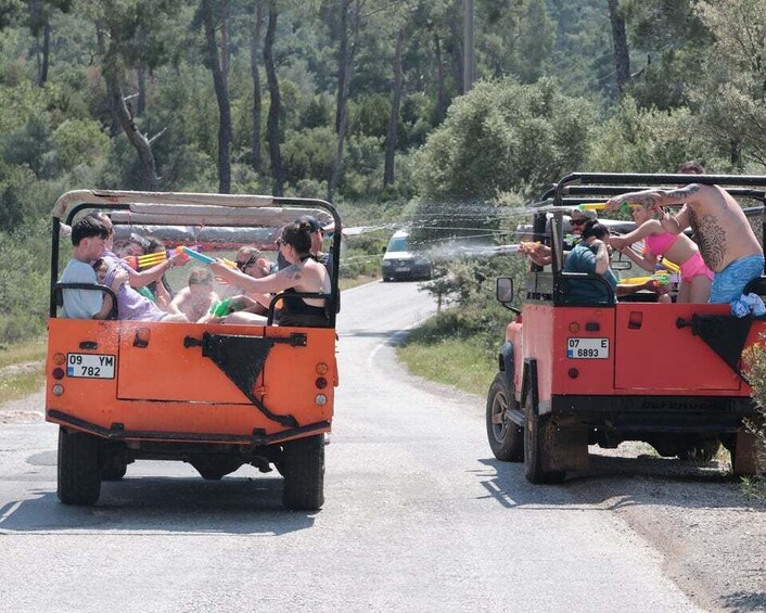 Two orange off-road vehicles on a rural road with passengers, surrounded by trees. 2