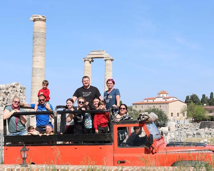 A group of people on a red vehicle near ancient ruins with columns. 1