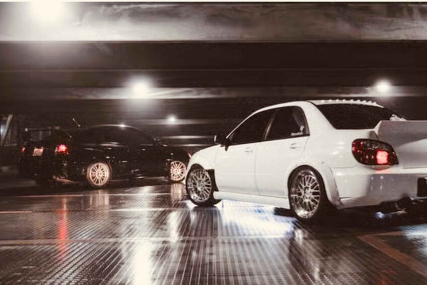 A white car parked in a dimly lit garage with other vehicles. 4
