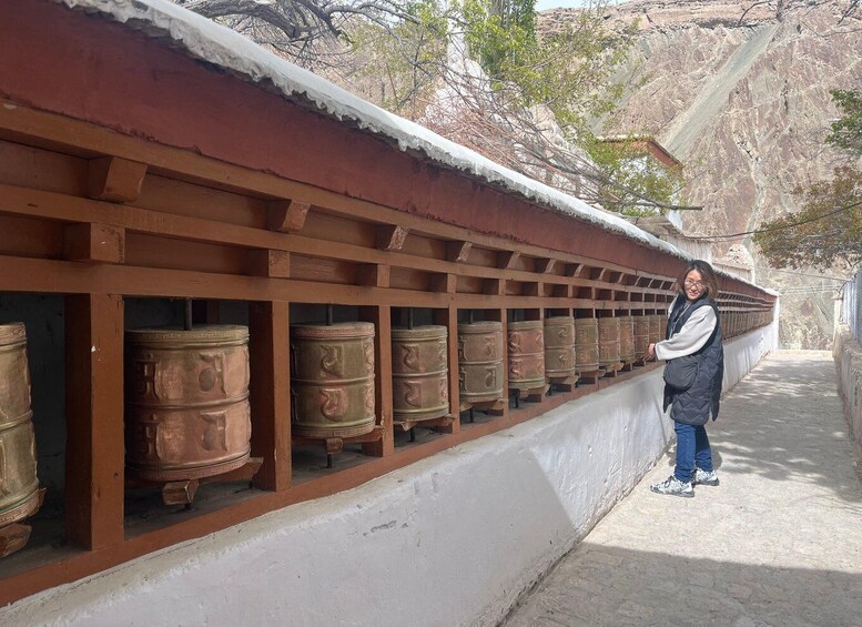 A person standing next to a row of large, ornate prayer wheels. 5