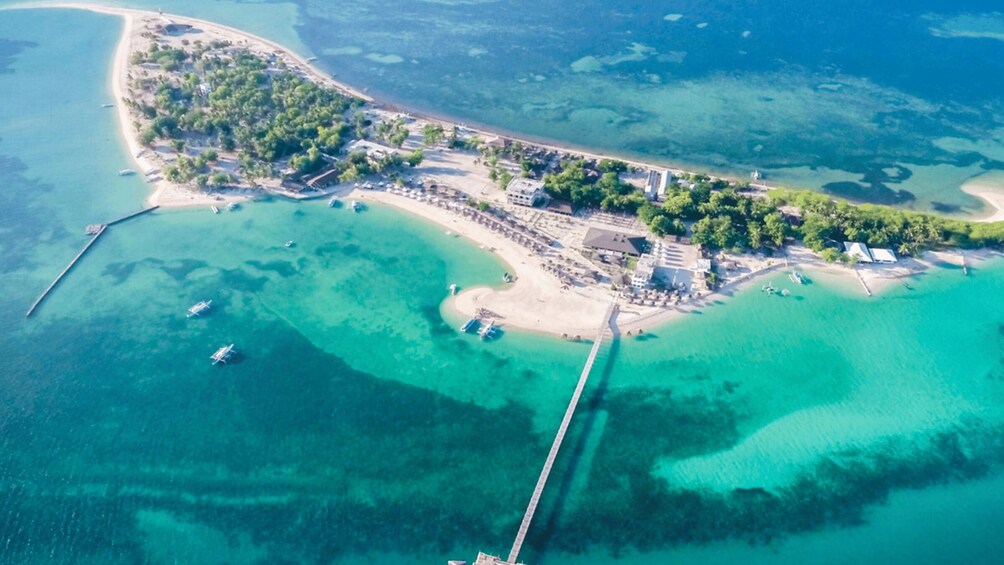 An aerial view of a coastal area with clear turquoise waters, a sandy beach, and a small island with buildings and vegetation. 3