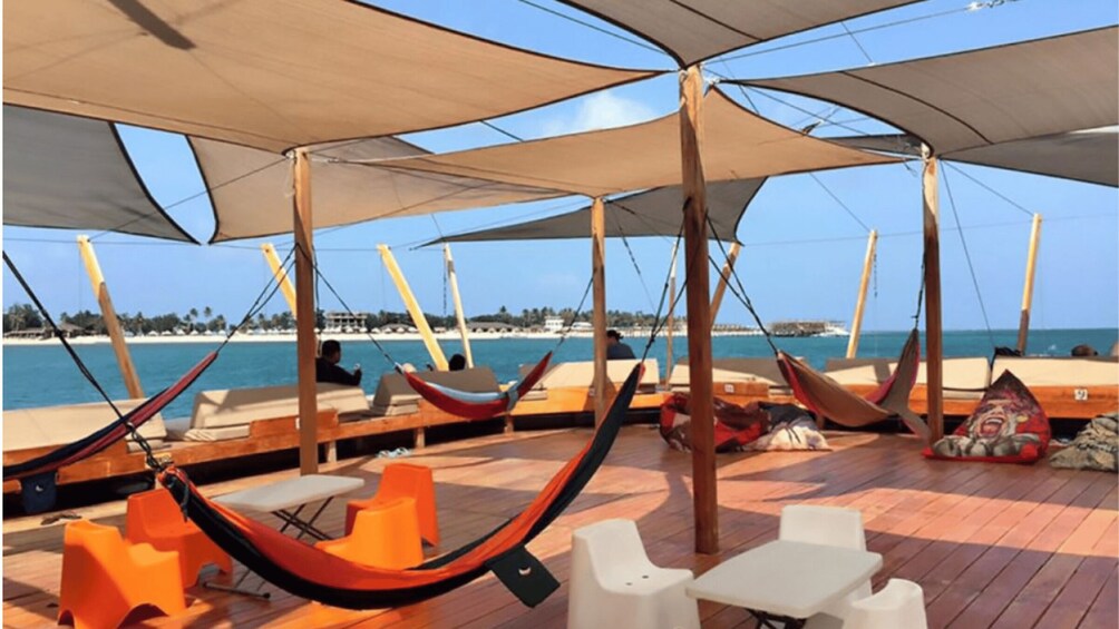A boat deck with hammocks, chairs, and tables, overlooking a beach and ocean. 2