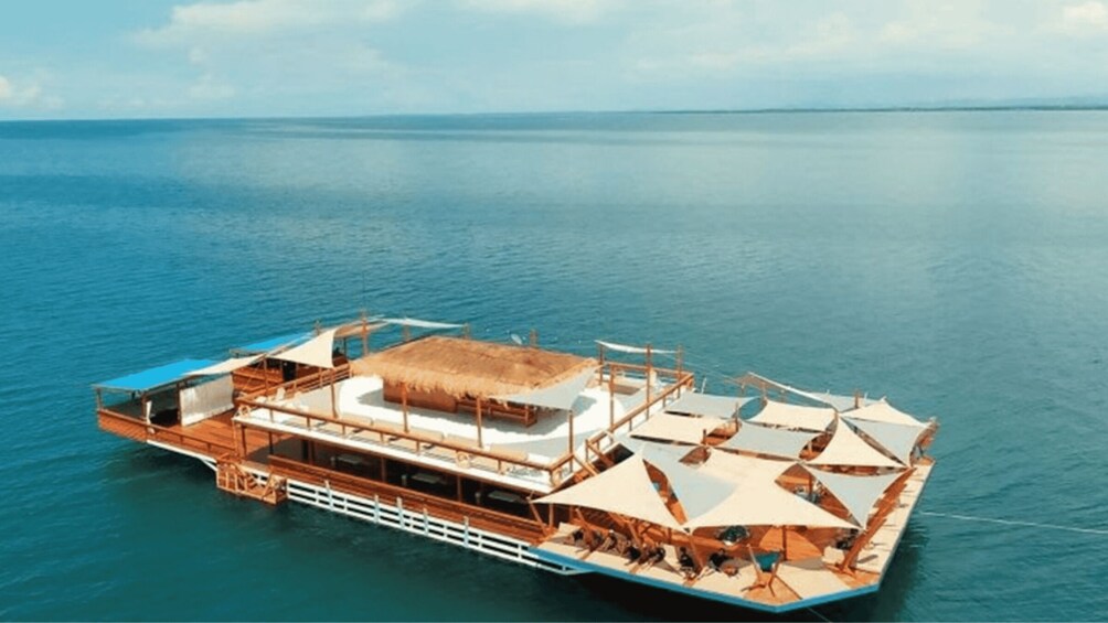 A floating structure with a thatched roof, wooden deck, and multiple umbrellas. 1