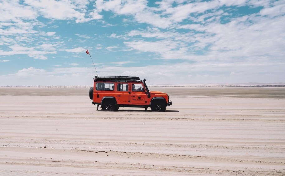 A red off-road vehicle on a flat, sandy terrain under a partly cloudy sky. 5