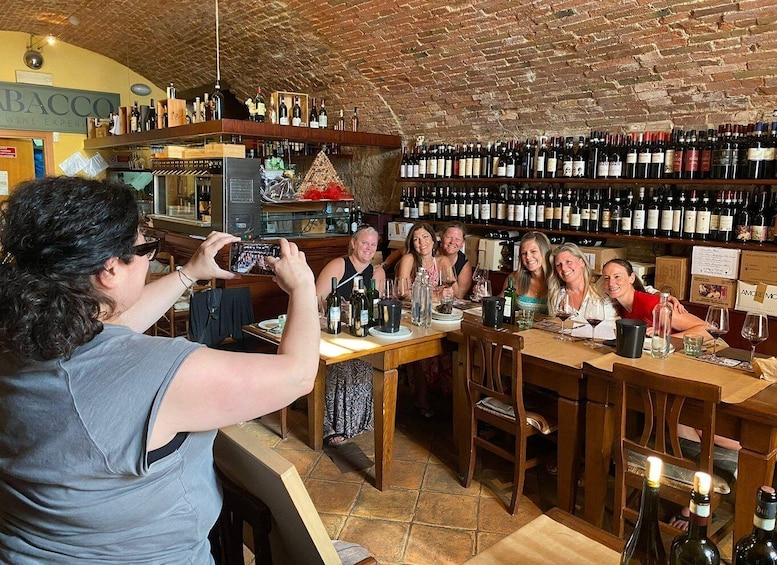 A group of people seated at a bar in a wine shop, with shelves of wine bottles behind them. 2