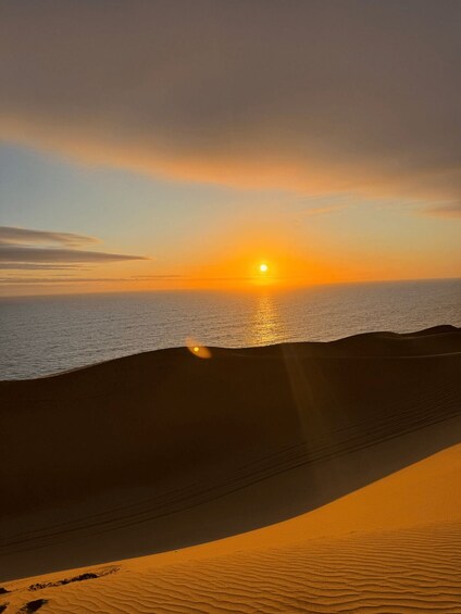 A sunset over a desert landscape with sand dunes and a calm sea. 1