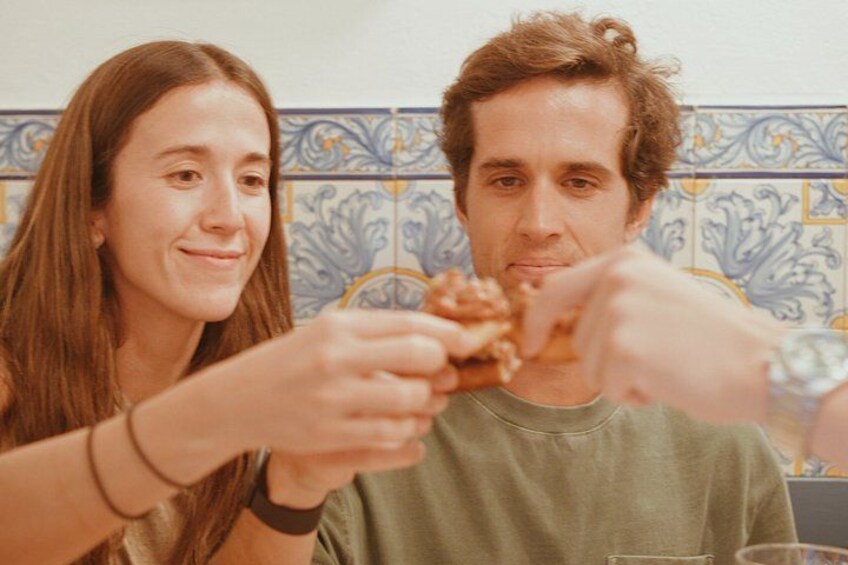 Two people sitting at a table, eating a piece of food. 5