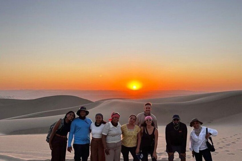 Een groep mensen staat op de duinen bij zonsondergang. 5