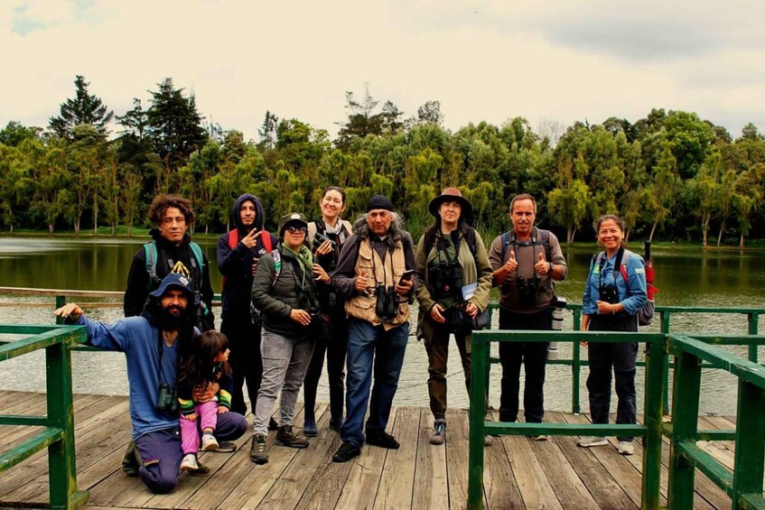 A group of people on a wooden dock by a lake with trees in the background. 4