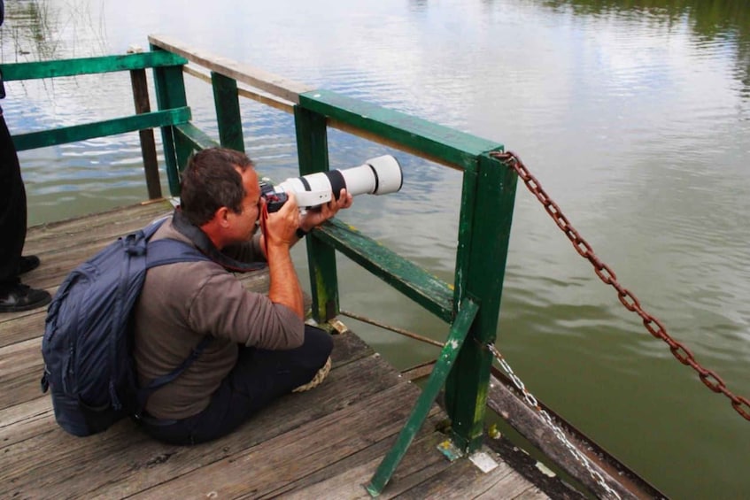 A person crouching on a wooden dock, taking a photograph with a large camera. 2