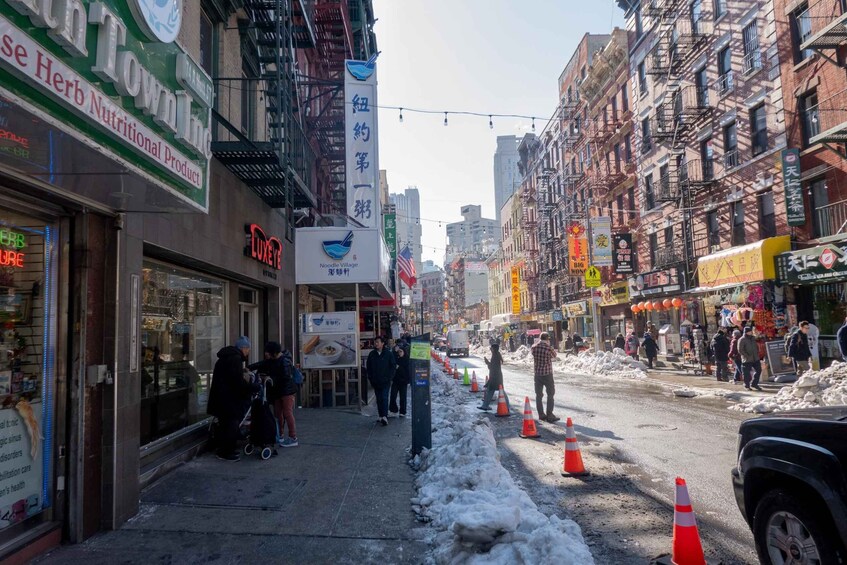 A snowy urban street with shops, pedestrians, and traffic cones. 2