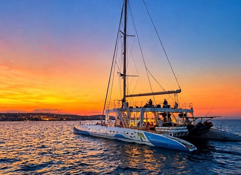 A sailboat with multiple decks and a mast, docked at sunset with a cityscape in the background. 2