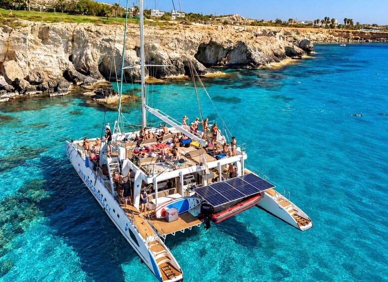 A sailboat with passengers enjoying the clear blue waters and rocky coastline. 1
