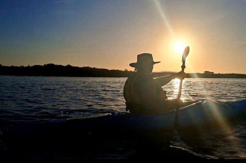 A person kayaking on a body of water during sunset. 1