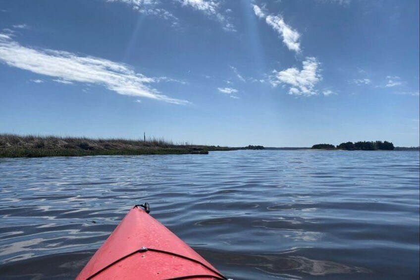 A calm body of water with a red kayak in the foreground and distant landforms under a clear sky. 3