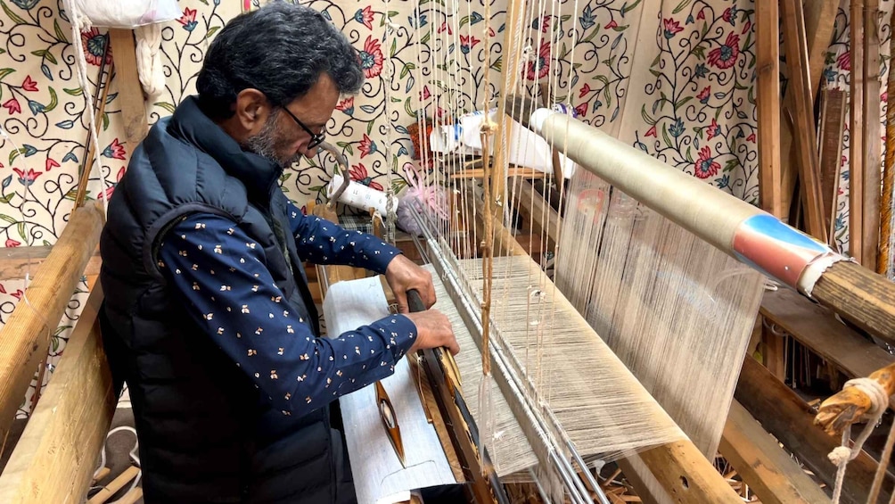 A person weaving on a loom with floral wallpaper in the background. 5
