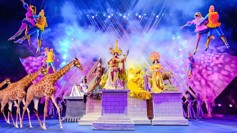 A stage with performers, a central statue, and giraffes. 1