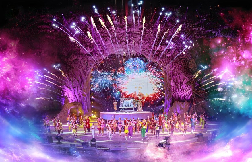 A stage with a large audience, surrounded by trees and a backdrop of fireworks. 4