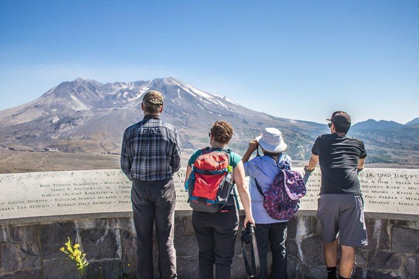 Four people standing on a ledge overlooking a mountain with inscriptions. 2