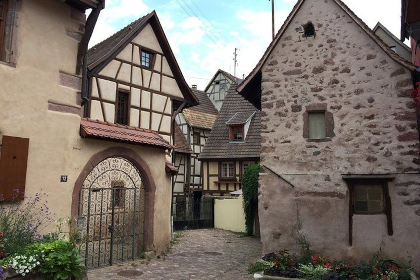 A narrow cobblestone street flanked by traditional half-timbered houses with a stone building on the right. 2
