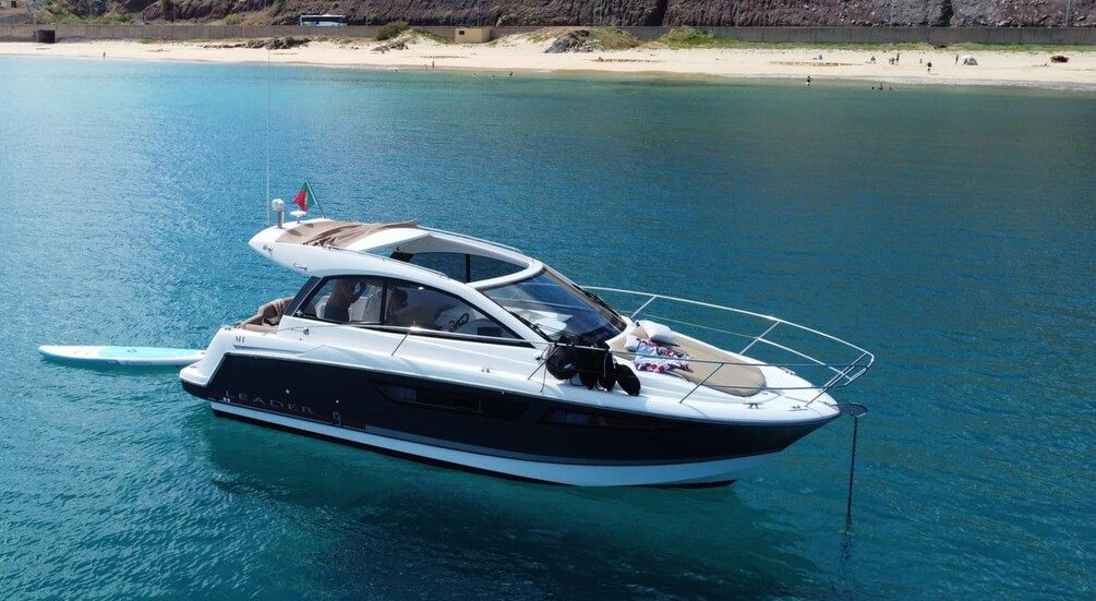 A boat named 'Leader' anchored near a beach with clear blue water. 1