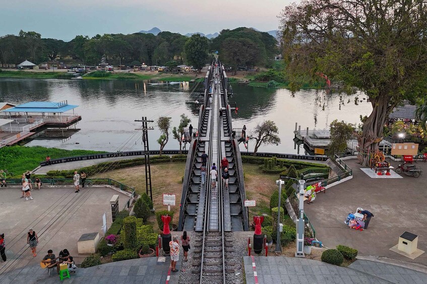 A pedestrian bridge over a river with people walking, a boat docked on the river, and a large tree on the right. 1